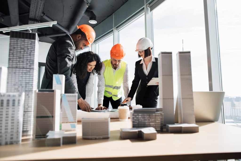 Group of four multiracial people architects standing near desk with lots of blueprints